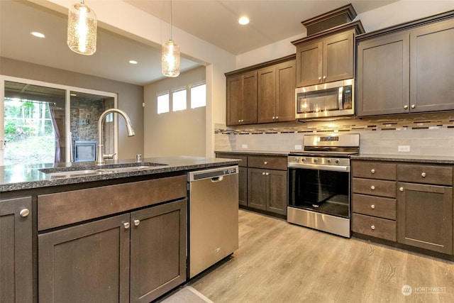 kitchen with pendant lighting, appliances with stainless steel finishes, sink, backsplash, and light wood-type flooring