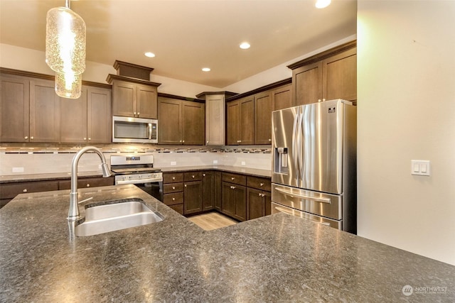 kitchen featuring appliances with stainless steel finishes, dark stone countertops, decorative backsplash, and hanging light fixtures