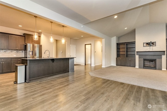 kitchen featuring vaulted ceiling, pendant lighting, decorative backsplash, an island with sink, and stainless steel fridge with ice dispenser