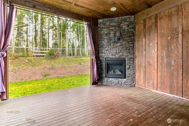 interior space featuring wooden ceiling, wood-type flooring, an outdoor stone fireplace, and wooden walls