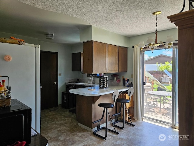 kitchen featuring a textured ceiling, a kitchen bar, hanging light fixtures, kitchen peninsula, and a chandelier