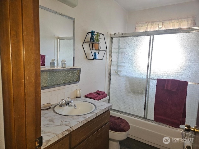 full bathroom featuring toilet, combined bath / shower with glass door, decorative backsplash, and vanity