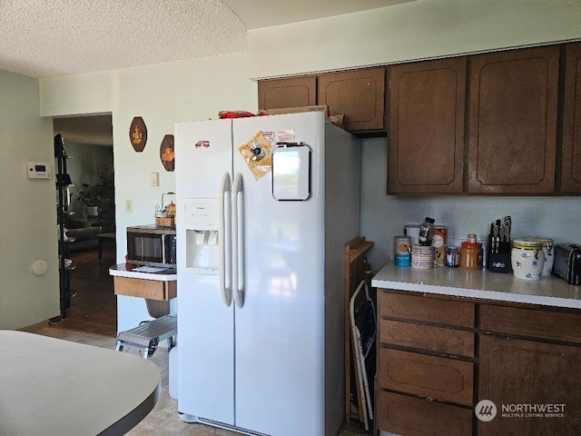 kitchen with dark brown cabinetry, white refrigerator with ice dispenser, and a textured ceiling