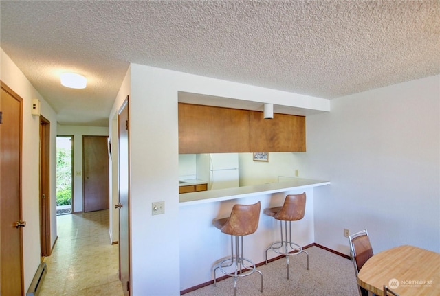 kitchen featuring kitchen peninsula, a kitchen breakfast bar, white refrigerator, and a textured ceiling