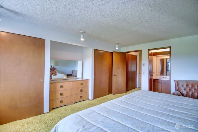 carpeted bedroom with ensuite bathroom, sink, and a textured ceiling