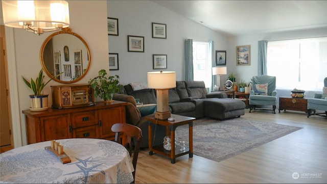 living room featuring plenty of natural light, a chandelier, vaulted ceiling, and light wood-type flooring