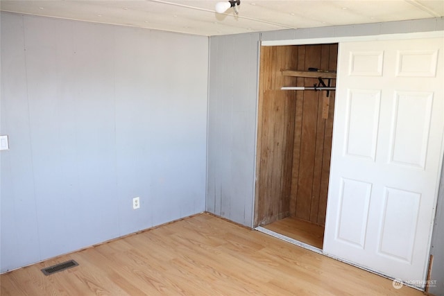 unfurnished bedroom with a closet, wooden walls, and light hardwood / wood-style floors