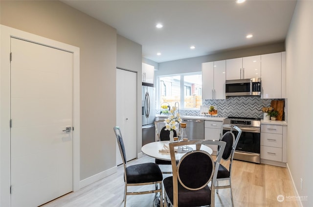 kitchen featuring appliances with stainless steel finishes, light wood-type flooring, white cabinetry, and backsplash