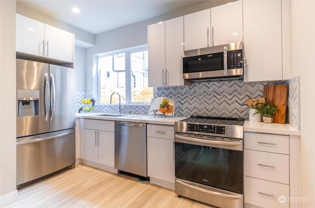 kitchen featuring backsplash, stainless steel appliances, sink, light hardwood / wood-style flooring, and white cabinetry