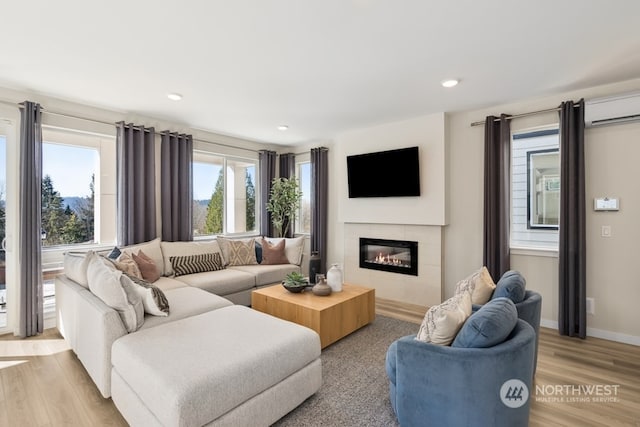 living room with a tiled fireplace, an AC wall unit, and light wood-type flooring