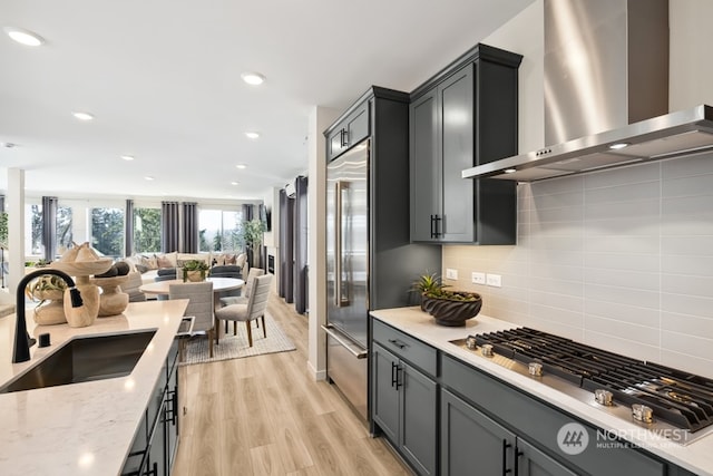 kitchen featuring sink, backsplash, stainless steel appliances, wall chimney range hood, and light wood-type flooring