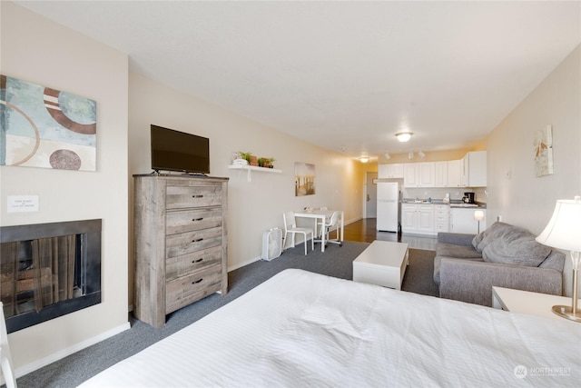 bedroom with a fireplace, freestanding refrigerator, and dark colored carpet