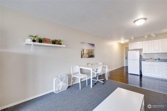 interior space with track lighting, a textured ceiling, dark colored carpet, baseboards, and dark wood-style flooring