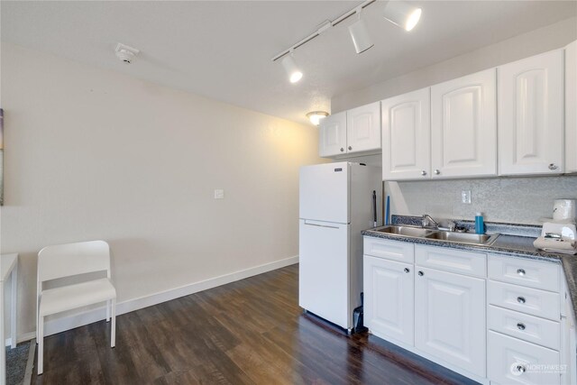 kitchen with white refrigerator, white cabinets, rail lighting, sink, and dark wood-type flooring