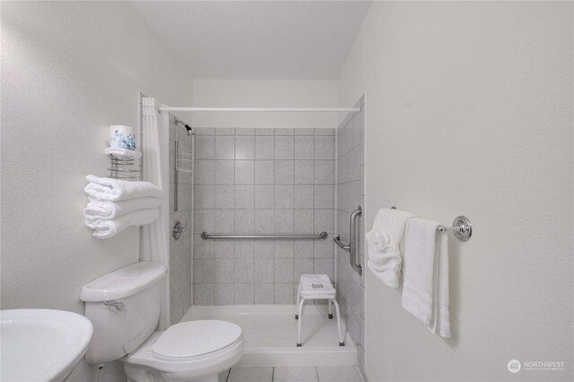 bathroom featuring tiled shower, sink, tile patterned flooring, and toilet