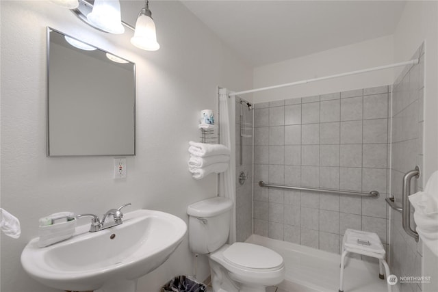 full bath featuring toilet, tiled shower, and a sink