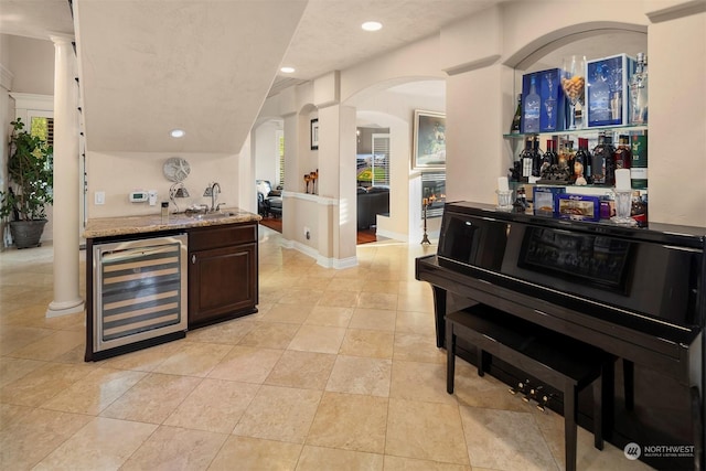 bar featuring sink, light tile patterned floors, dark brown cabinets, light stone counters, and beverage cooler