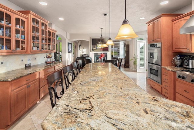 kitchen with light stone countertops, decorative light fixtures, a breakfast bar area, light tile patterned floors, and appliances with stainless steel finishes