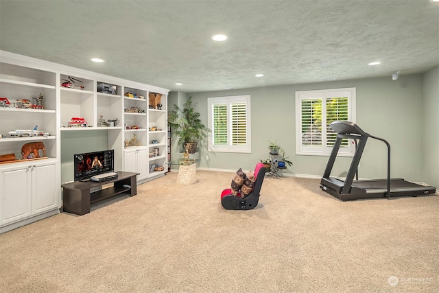 exercise room with light colored carpet and a textured ceiling