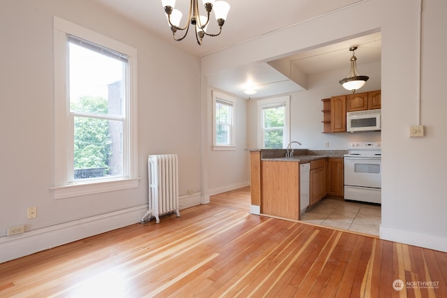 kitchen featuring a wealth of natural light, radiator, white appliances, pendant lighting, and light tile flooring