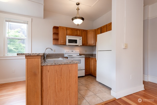 kitchen featuring white appliances, kitchen peninsula, light stone counters, sink, and light tile floors