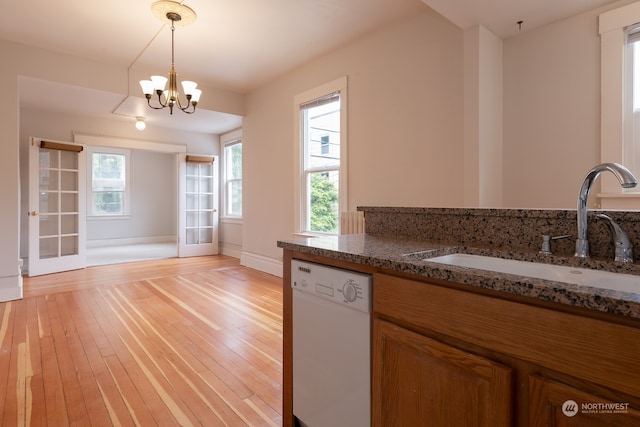 kitchen with white dishwasher, light hardwood / wood-style floors, sink, and dark stone countertops