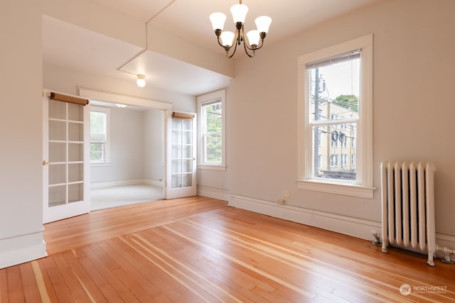 empty room featuring light hardwood / wood-style floors, french doors, radiator, and a notable chandelier