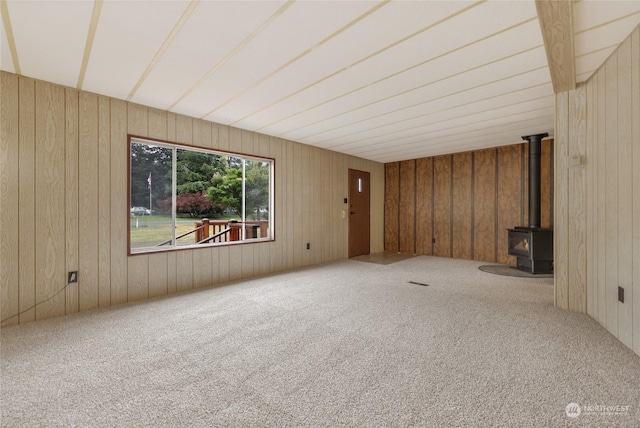 unfurnished living room with wooden walls, carpet flooring, and a wood stove