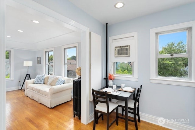 living room featuring radiator, light hardwood / wood-style floors, a wall mounted AC, and a healthy amount of sunlight