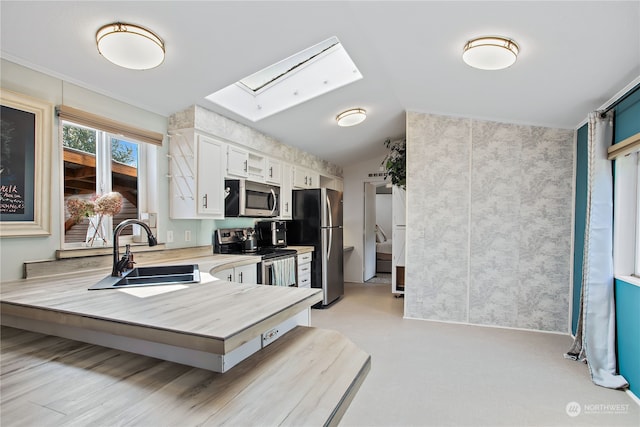kitchen with lofted ceiling with skylight, a sink, light countertops, white cabinets, and appliances with stainless steel finishes