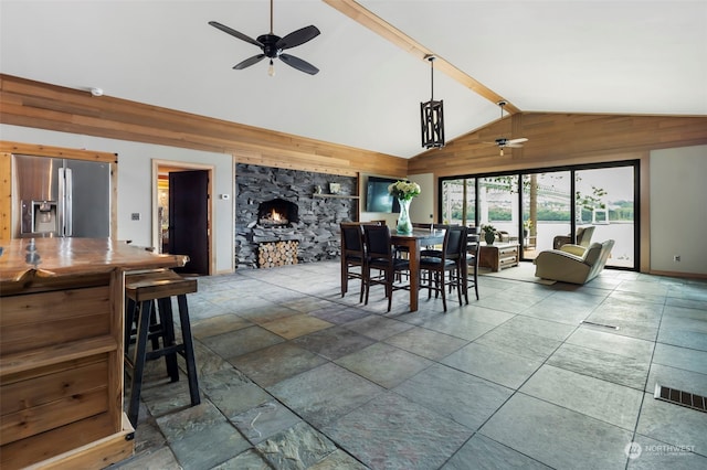 dining area featuring lofted ceiling with beams, a stone fireplace, and ceiling fan