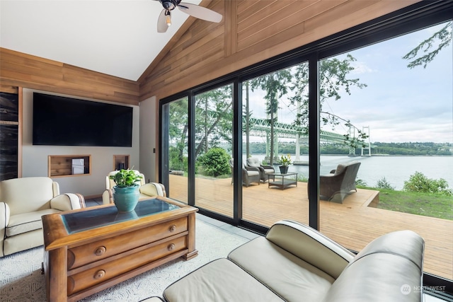 living room with ceiling fan, wood walls, a water view, and vaulted ceiling