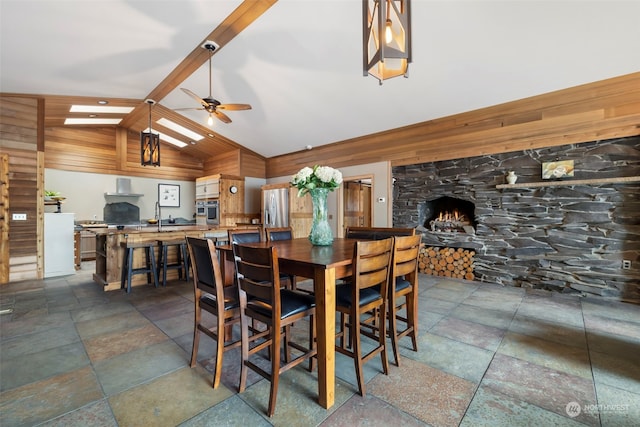 dining room featuring a stone fireplace, lofted ceiling with skylight, and ceiling fan