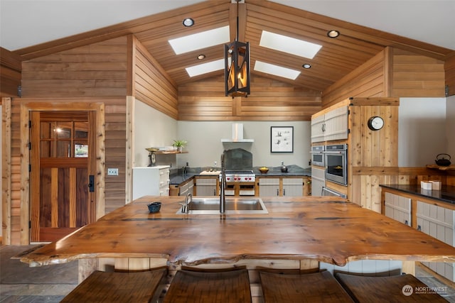 dining room featuring a skylight, high vaulted ceiling, wooden walls, and sink