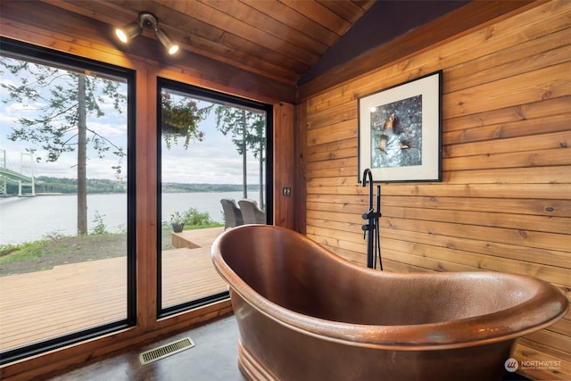 interior space featuring wooden walls, a bath, a water view, wooden ceiling, and lofted ceiling