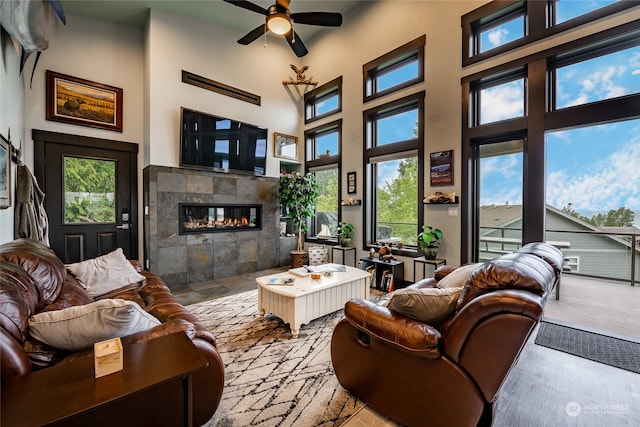 living room with a towering ceiling, a tiled fireplace, and ceiling fan