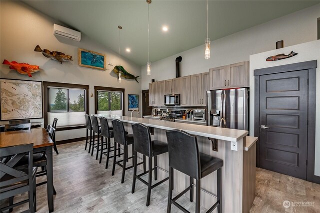 kitchen with stainless steel appliances, pendant lighting, light hardwood / wood-style floors, an island with sink, and high vaulted ceiling