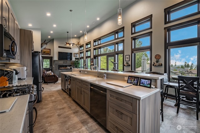 kitchen featuring appliances with stainless steel finishes, sink, wood-type flooring, a tile fireplace, and a center island with sink