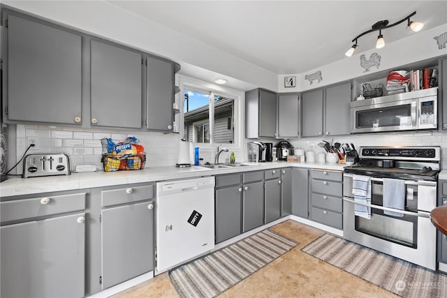 kitchen featuring appliances with stainless steel finishes, gray cabinets, tasteful backsplash, and sink