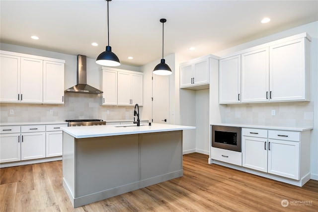 kitchen with built in microwave, sink, hanging light fixtures, wall chimney range hood, and white cabinets