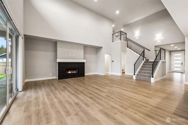 unfurnished living room with a tile fireplace, a high ceiling, light hardwood / wood-style floors, and a wealth of natural light