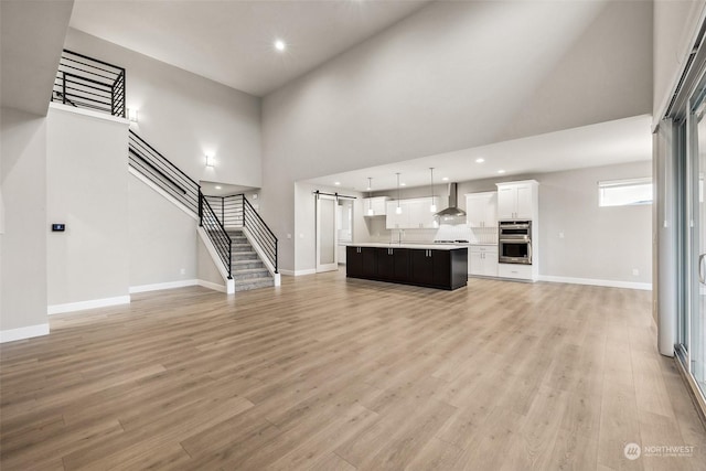 unfurnished living room featuring a barn door, light hardwood / wood-style floors, sink, and a high ceiling