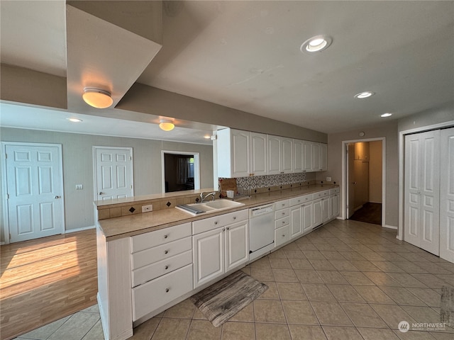 kitchen featuring kitchen peninsula, light tile flooring, white dishwasher, sink, and white cabinets