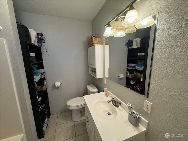 bathroom with vanity, toilet, a textured wall, and tile patterned floors