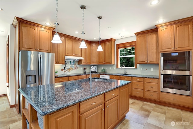 kitchen featuring stainless steel appliances, decorative light fixtures, sink, and an island with sink