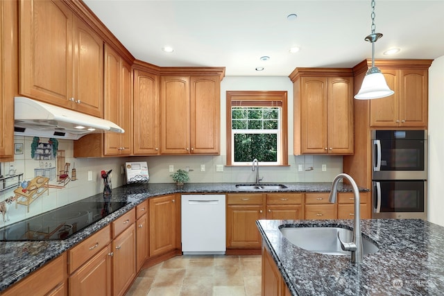 kitchen featuring tasteful backsplash, dark stone counters, white dishwasher, hanging light fixtures, and sink