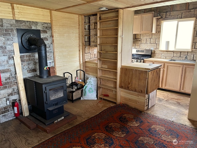 kitchen featuring light wood-type flooring, range with gas cooktop, a wood stove, sink, and light brown cabinets