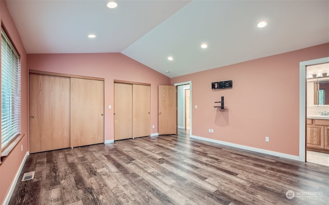 unfurnished bedroom with vaulted ceiling, hardwood / wood-style flooring, multiple windows, two closets, and ensuite bath