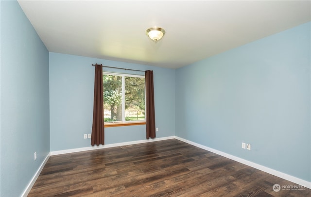 spare room with dark wood-type flooring, visible vents, and baseboards