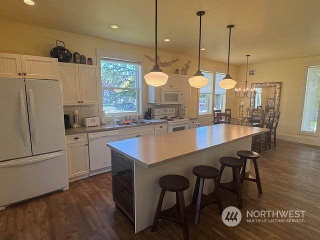 kitchen featuring a kitchen bar, white cabinetry, a kitchen island, pendant lighting, and white appliances